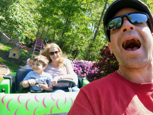 Mike and his family on a roller coaster, Mike in the foreground, and his wife and son in the car behind him.